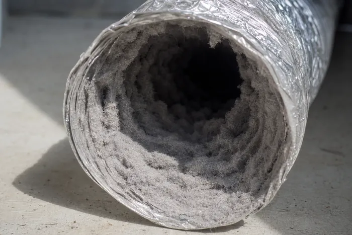 The mouth of a flexible dryer duct choked with a thick blanket of packed grey lint